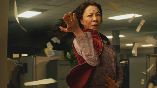 A screencap from the movie Everything Everywhere All at Once showing Evelyn (played by Michelle Yeoh) standing in a fighting pose in the middle of a sea of office cubicles. A single googly eye is stuck to her forehead.